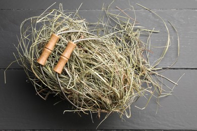 Dried hay in metal basket on grey wooden table, top view