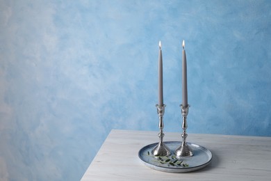 Photo of Holders with burning candles on wooden table near light blue wall, space for text