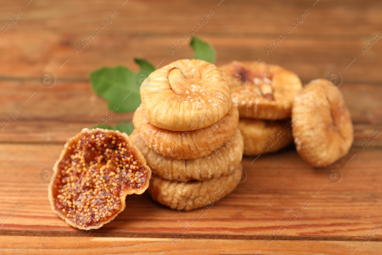 Photo of Tasty dried figs and green leaf on wooden table, closeup