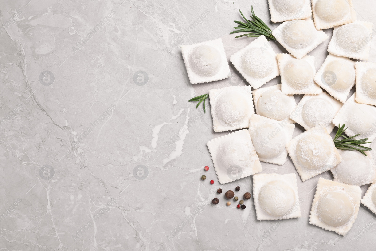 Photo of Uncooked ravioli, rosemary and peppercorns on grey marble table, flat lay. Space for text