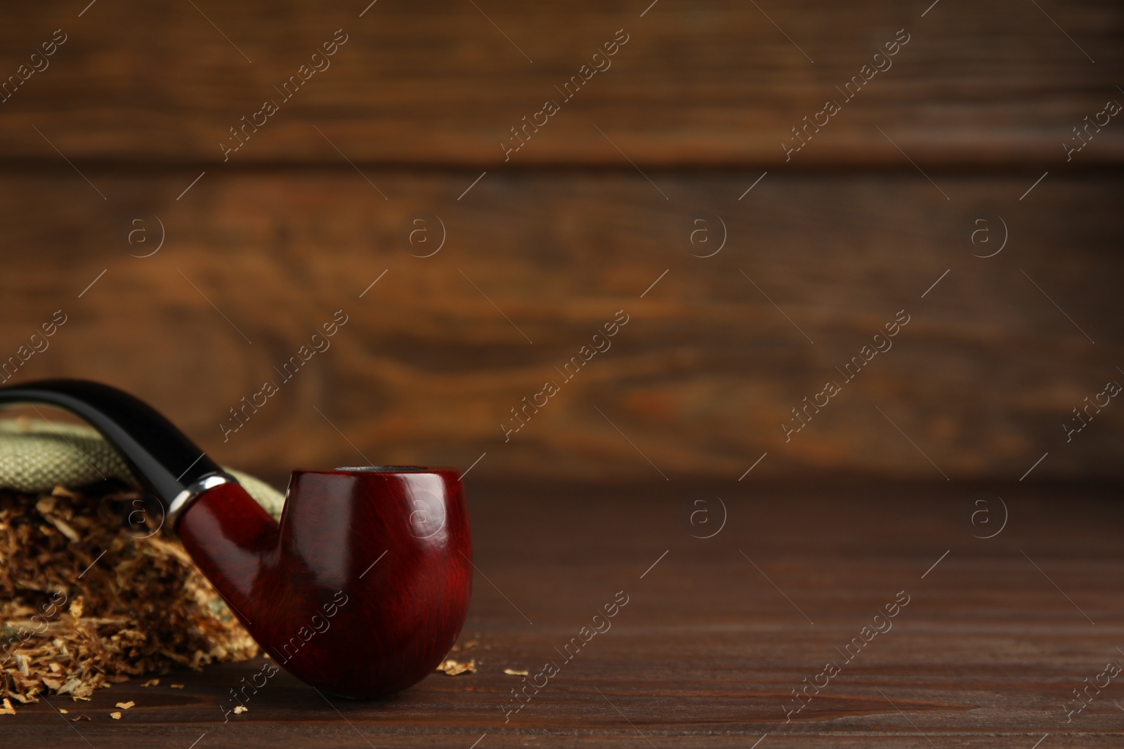 Photo of Classic smoking pipe with sack of tobacco on wooden table. Space for text