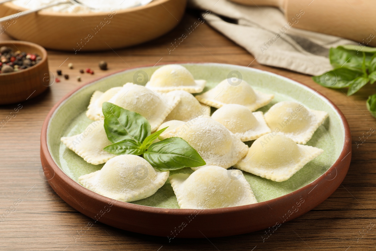Photo of Uncooked ravioli and basil on wooden table