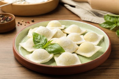 Photo of Uncooked ravioli and basil on wooden table