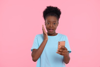 Photo of Shocked young woman with smartphone on pink background