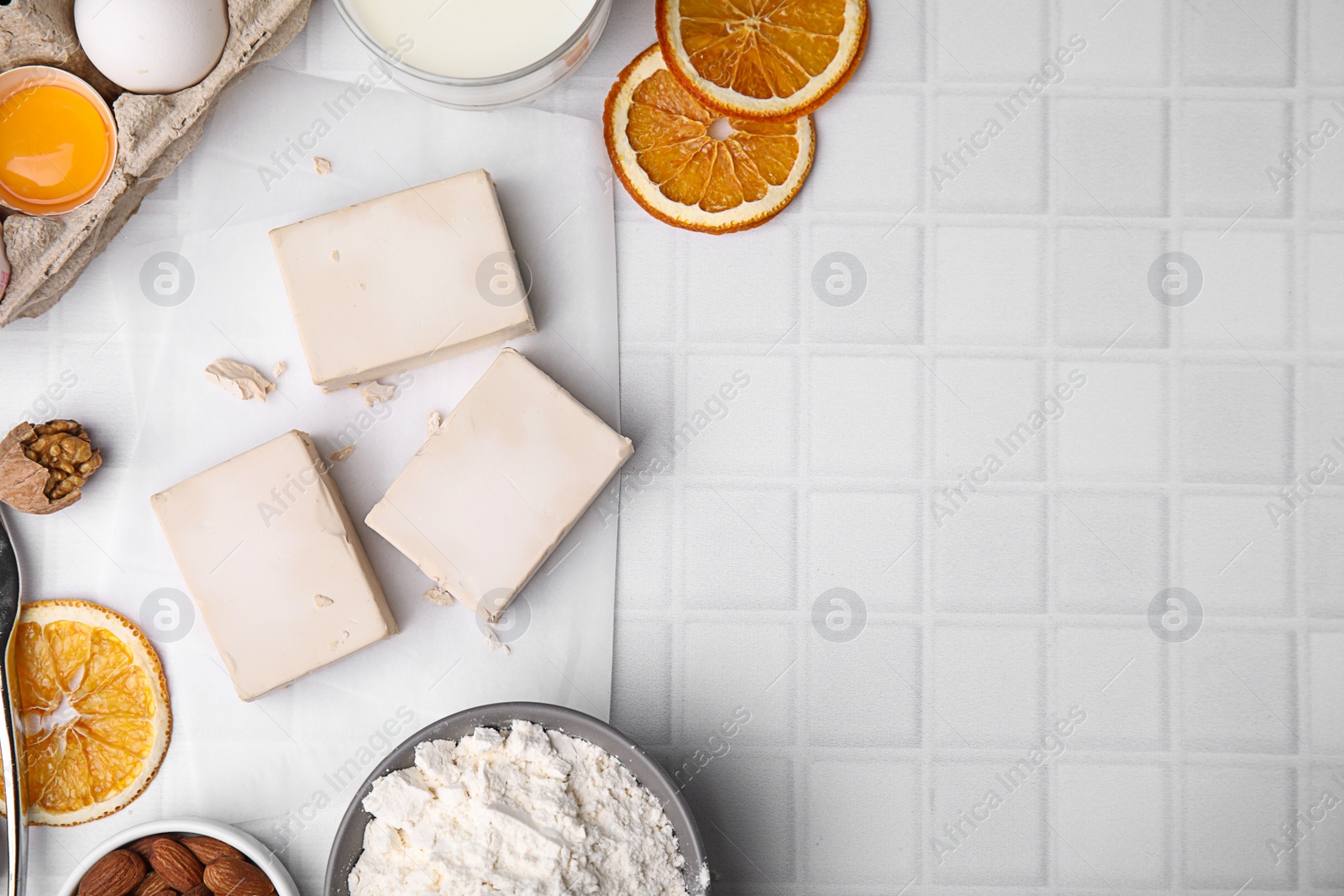 Photo of Yeast and ingredients for dough on white tiled table, flat lay. Space for text