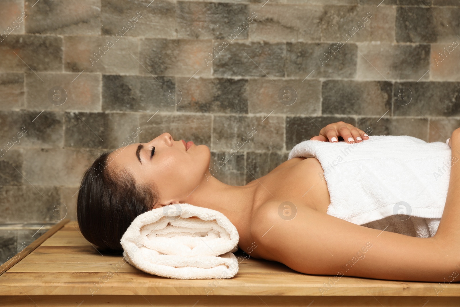 Photo of Young woman lying on wooden bench in salt sauna. Spa treatment