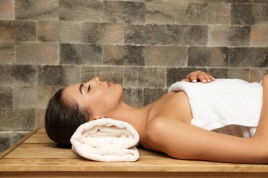 Photo of Young woman lying on wooden bench in salt sauna. Spa treatment