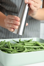 Woman adding spices to green beans at white table, closeup