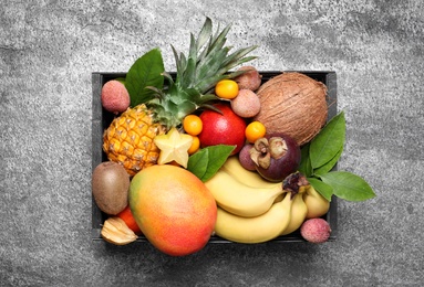 Different tropical fruits in wooden box on grey background, top view