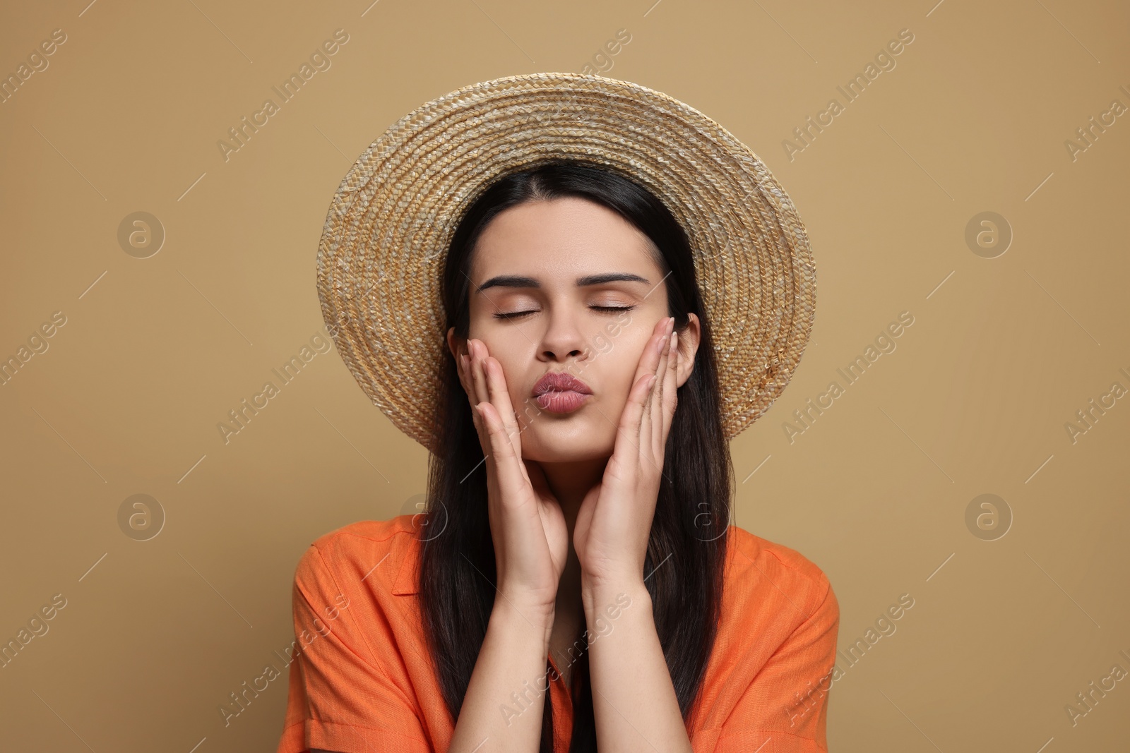 Photo of Beautiful young woman in straw hat giving kiss on beige background