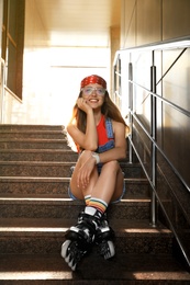 Photo of Beautiful young woman with roller skates sitting on stairs outdoors