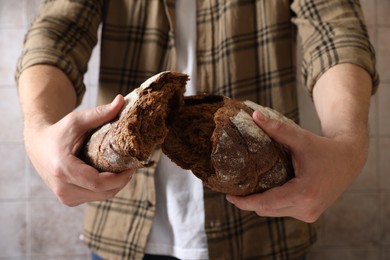 Man breaking loaf of fresh bread near grey wall, closeup