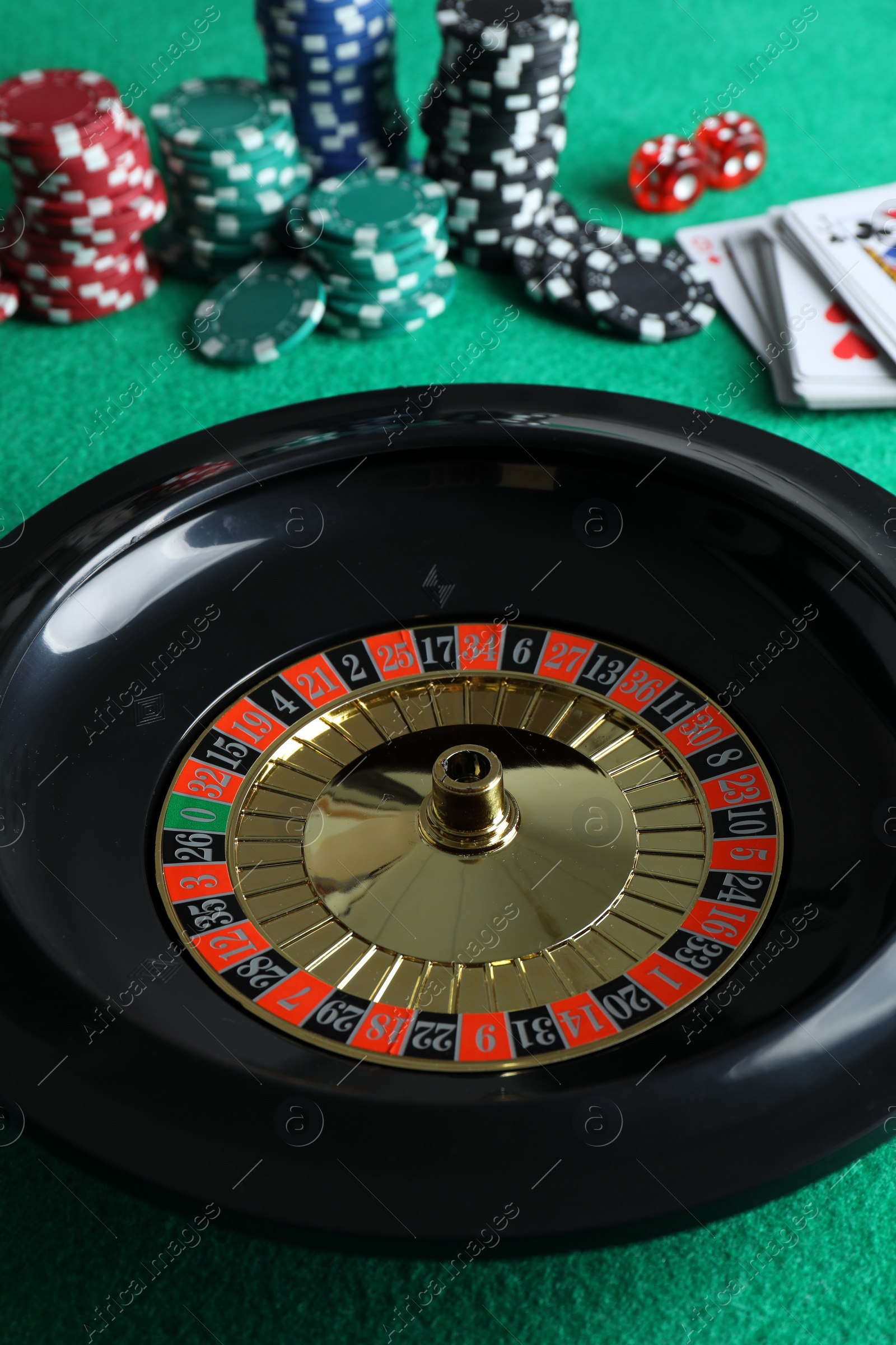 Photo of Roulette wheel with ball, playing cards and chips on green table, closeup. Casino game