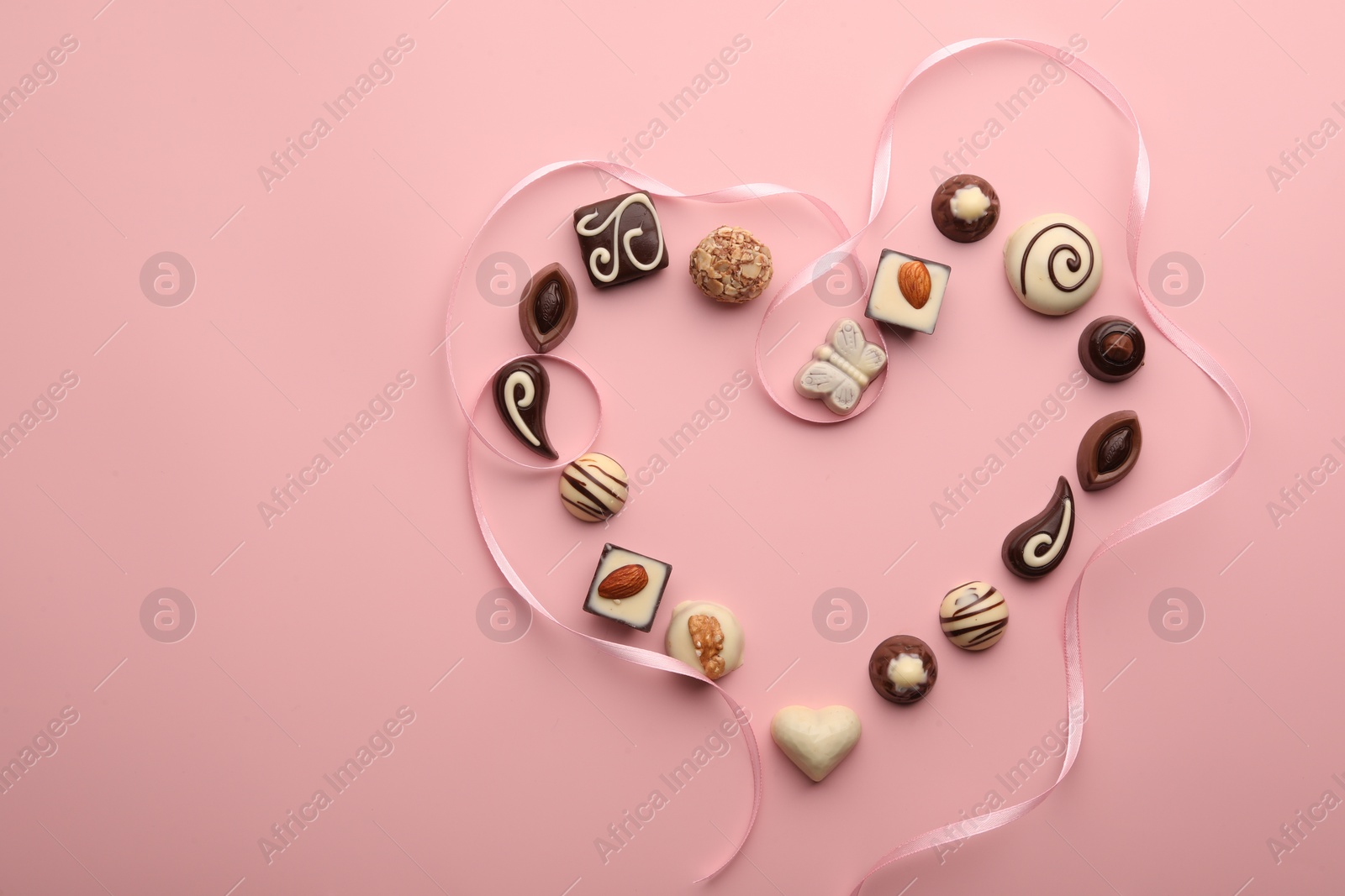 Photo of Heart made with delicious chocolate candies on light pink background, flat lay. Space for text