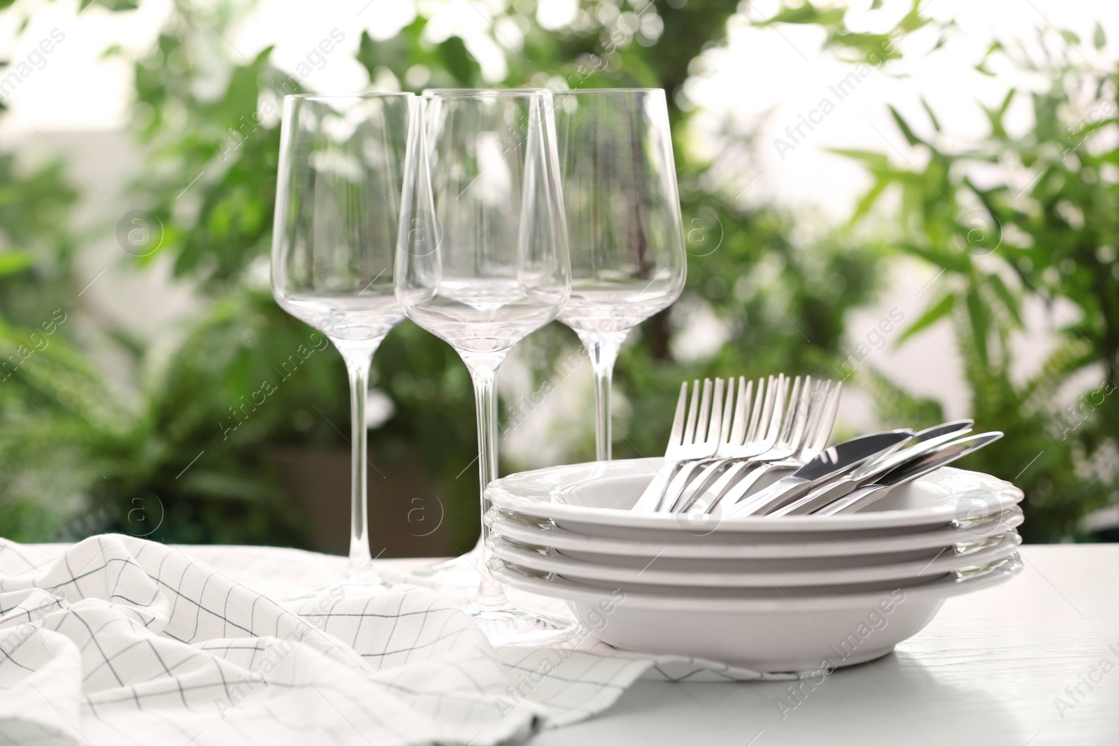 Photo of Set of clean dishware, cutlery and wineglasses on white table against blurred background