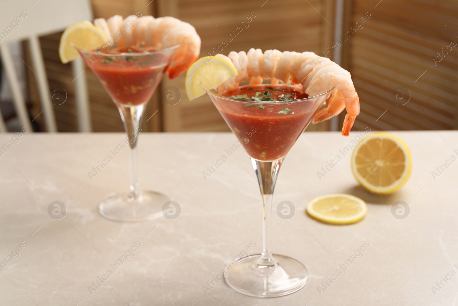 Photo of Tasty shrimp cocktail with sauce in glasses and lemon on light marble table