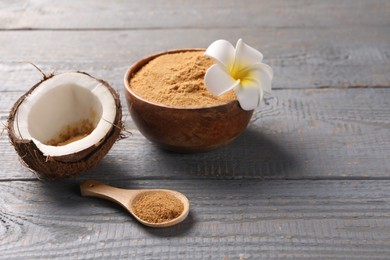 Photo of Coconut sugar, bowl, spoon, flower and fruit on grey wooden table. Space for text