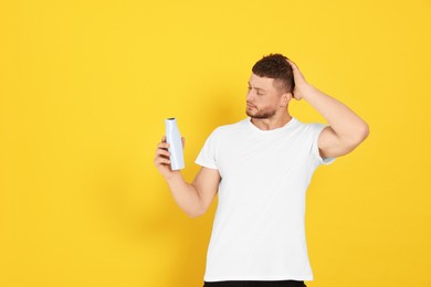 Handsome young man holding bottle of shampoo on orange background, space for text