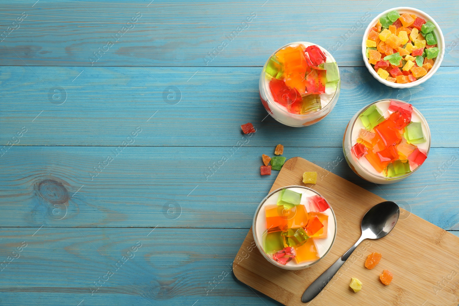 Photo of Delicious broken glass jelly dessert on light blue wooden table, flat lay. Space for text