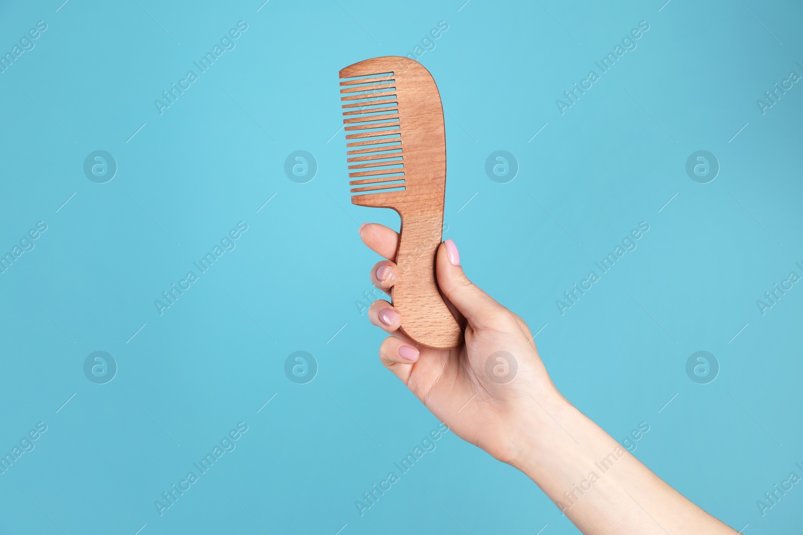 Photo of Woman holding wooden hair comb against blue background, closeup. Space for text