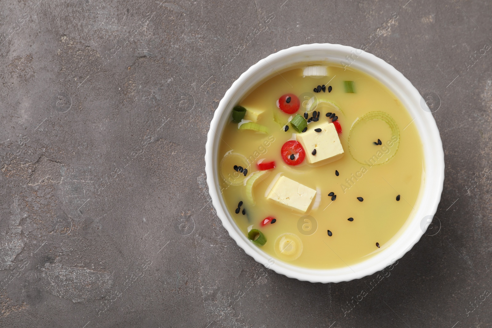 Photo of Bowl of delicious miso soup with tofu on grey table, top view. Space for text