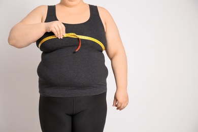 Photo of Overweight woman with measuring tape on light background