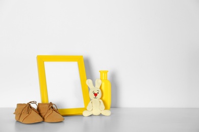 Photo of Composition with photo frame and bootees for baby room interior on table near white wall