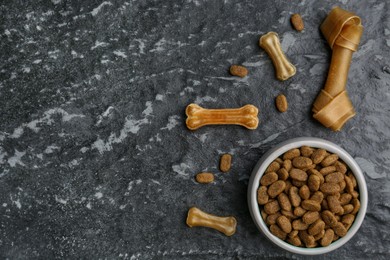 Photo of Dry dog food and treats (chew bones) on black textured background, flat lay. Space for text