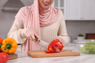 Muslim woman making delicious salad with vegetables at white table in kitchen, closeup