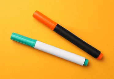 Photo of Bright color markers on orange background, flat lay