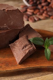 Pieces of tasty milk chocolate and mint on wooden table, closeup