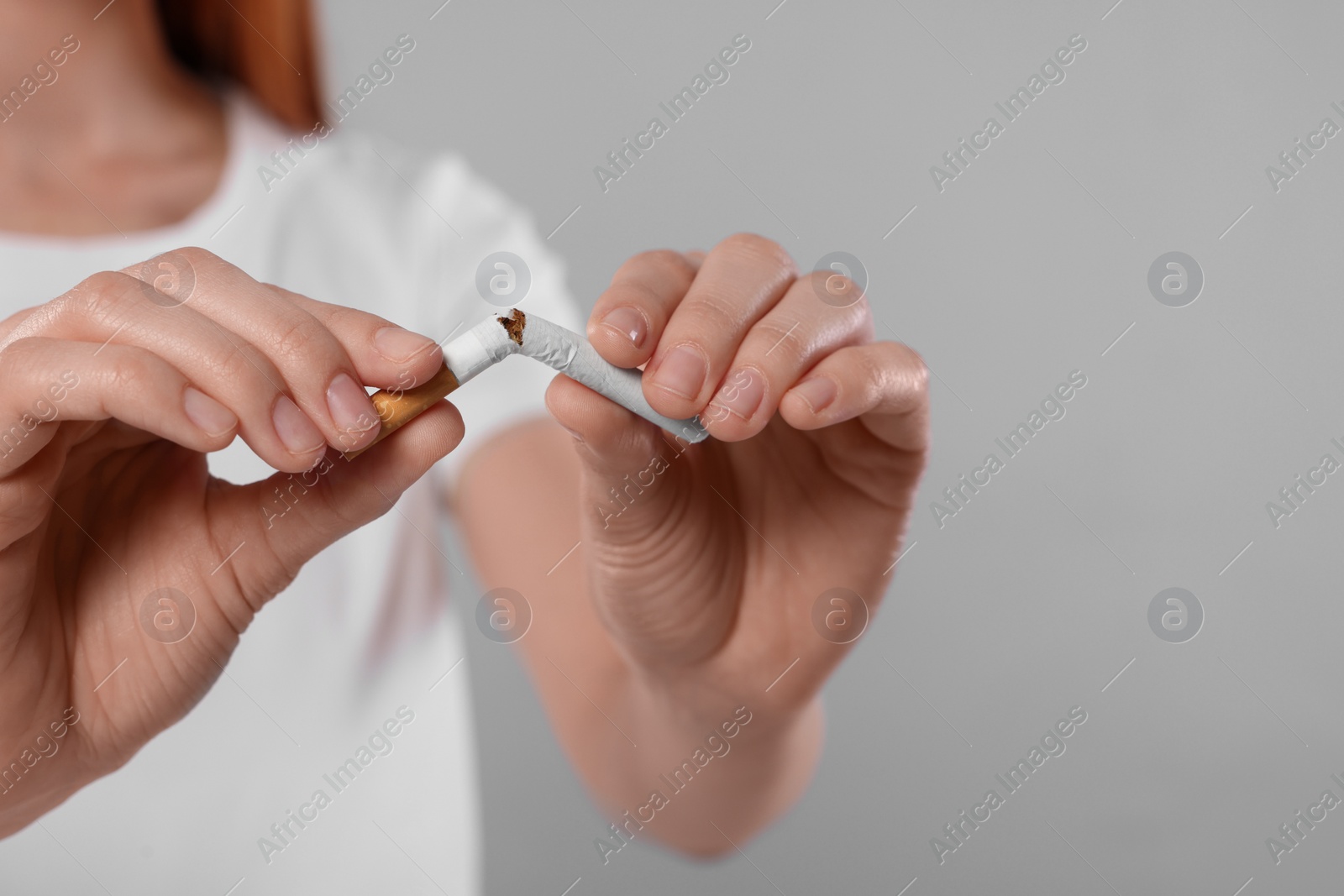 Photo of Stop smoking concept. Woman breaking cigarette on light gray background, closeup with space for text