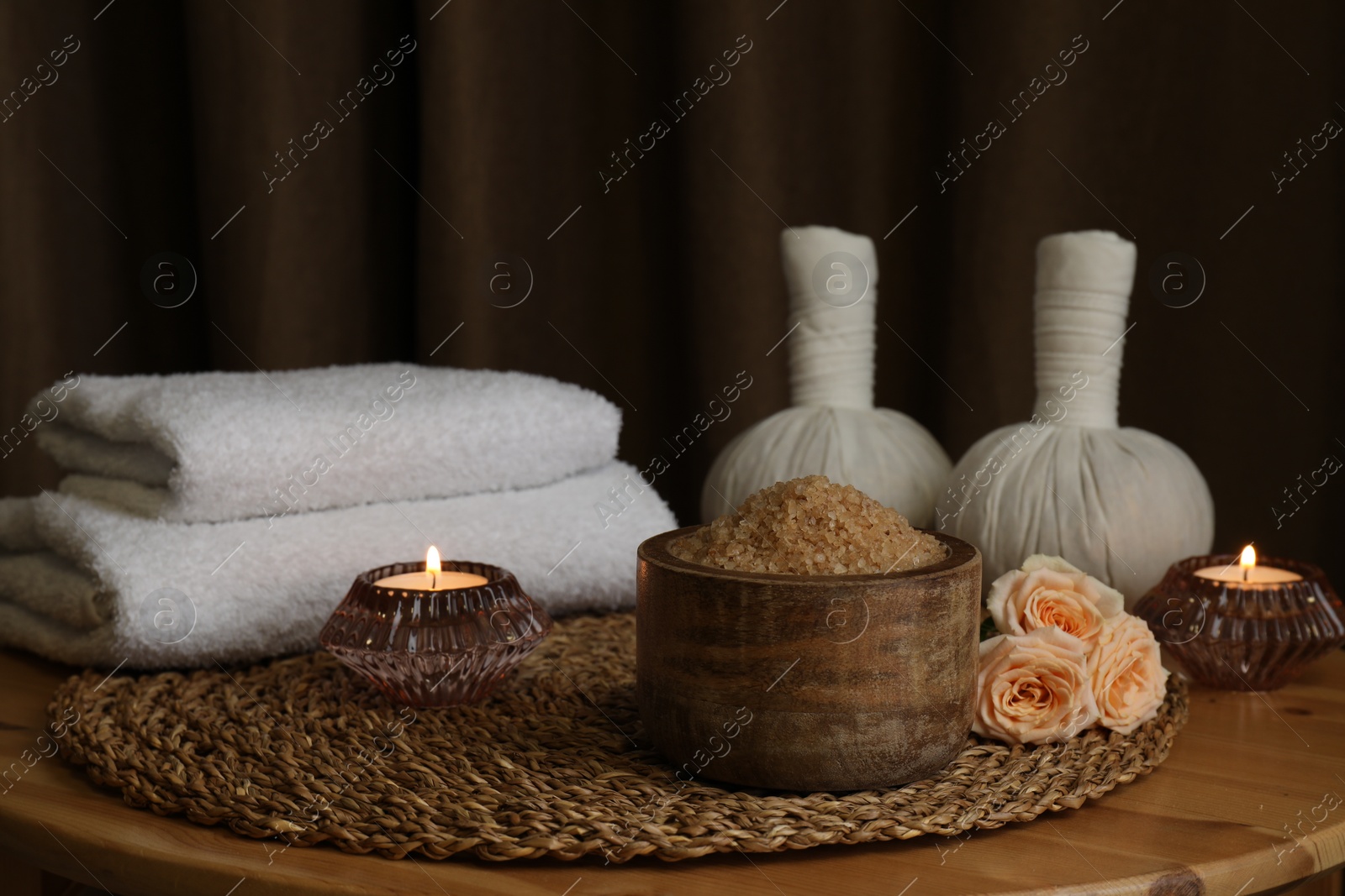 Photo of Bowl of sea salt, roses, burning candles and towels on wooden table