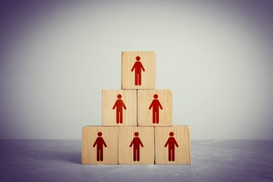 Team and management concept. Pyramid of wooden cubes with human icons on table