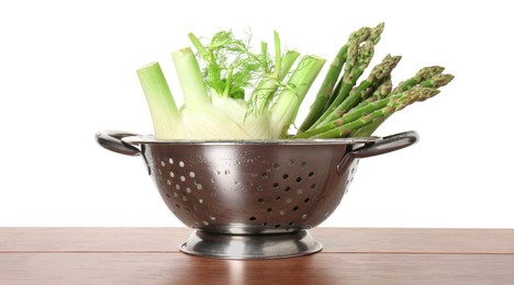 Metal colander with fennel and asparagus on wooden table against white background