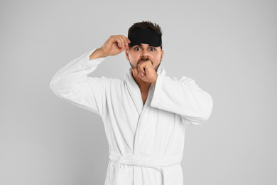 Photo of Young man in bathrobe and eye sleeping mask on light grey background