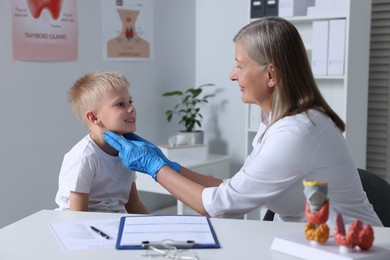 Photo of Endocrinologist examining boy's thyroid gland at table in hospital
