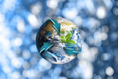 Image of Recycling concept. Earth planet with light blue arrows and green leaves on blurred background, illustration