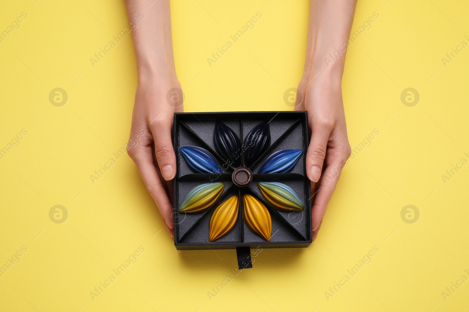 Photo of Woman with box of delicious chocolate candies on yellow background, top view