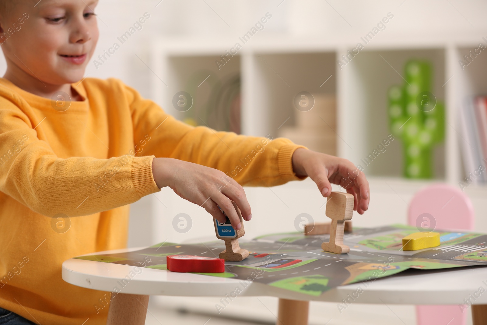 Photo of Cute little boy playing with set of wooden road signs and cars at table indoors, closeup. Child's toy