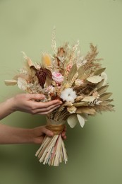 Photo of Woman holding beautiful dried flower bouquet on green background, closeup