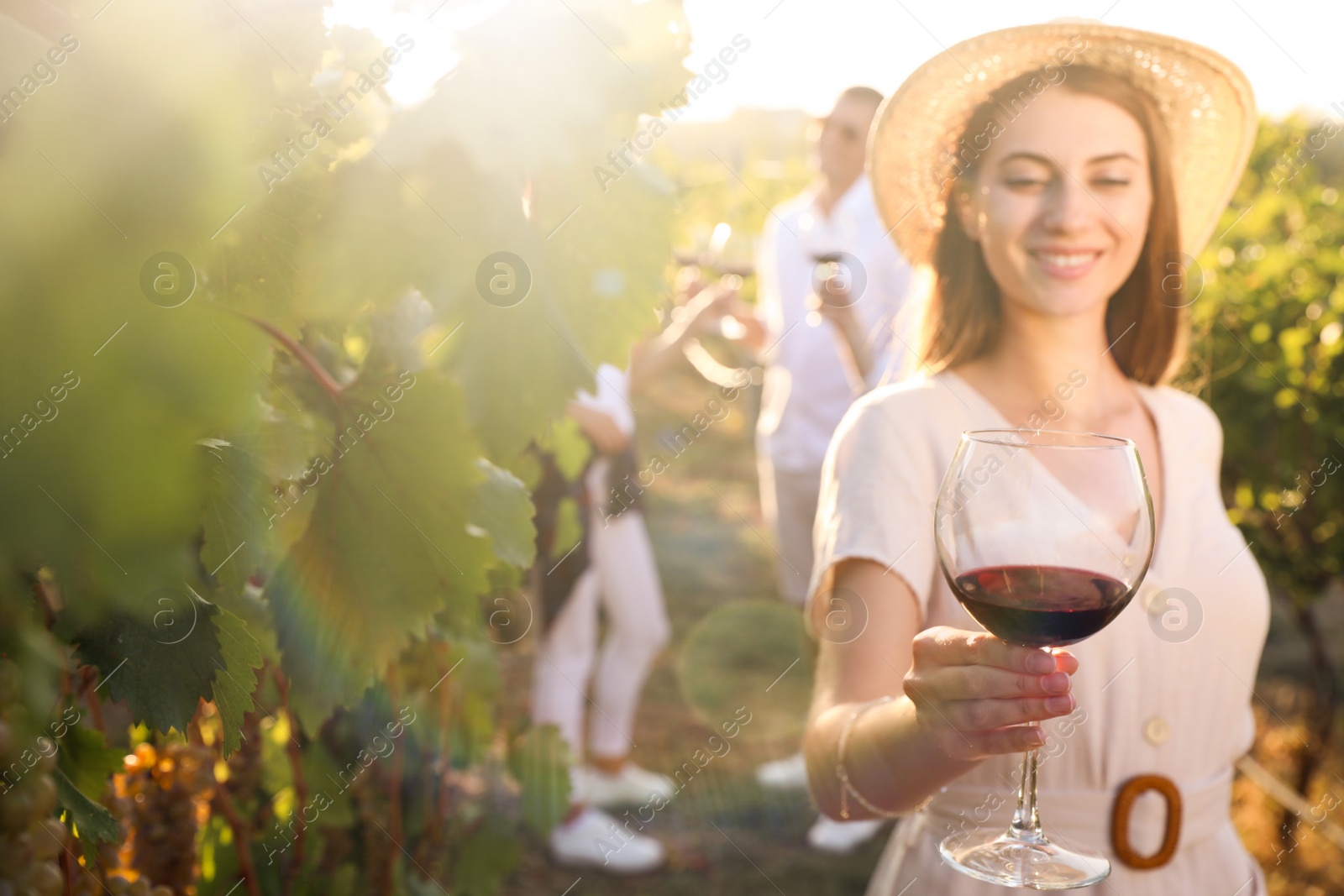 Photo of Beautiful young woman with glass of wine in vineyard, focus on hand