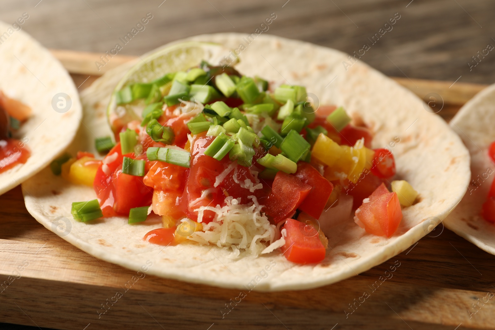 Photo of Delicious taco with vegetables, green onion, lime and ketchup on table, closeup