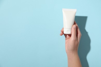 Woman with tube of hand cream on light blue background, top view. Space for text