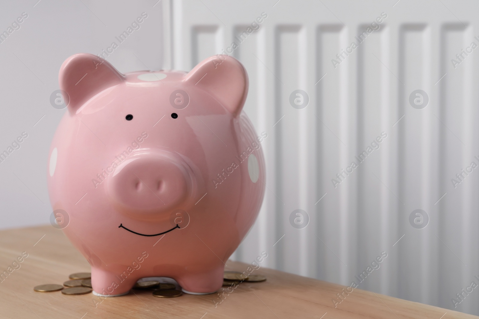 Photo of Piggy bank on wooden table near heating radiator, space for text