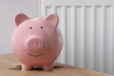 Photo of Piggy bank on wooden table near heating radiator, space for text