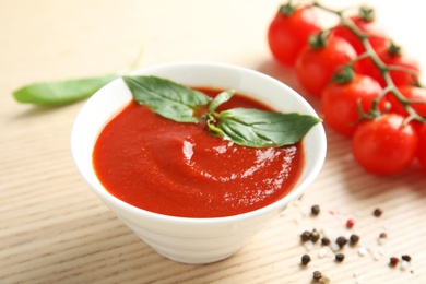 Photo of Bowl of tasty tomato sauce with basil on wooden table