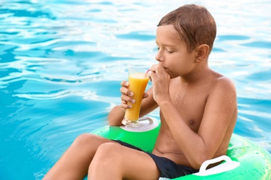 Happy cute boy drinking juice on inflatable ring in swimming pool