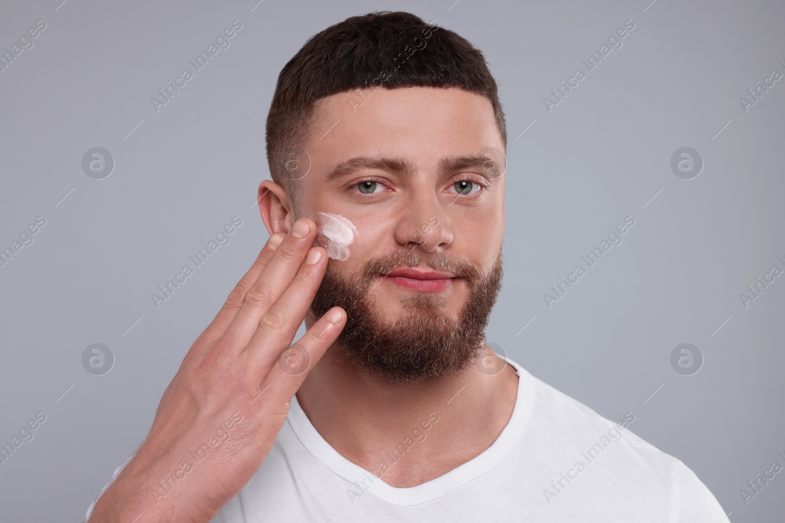 Photo of Handsome man applying cream onto his face on light grey background