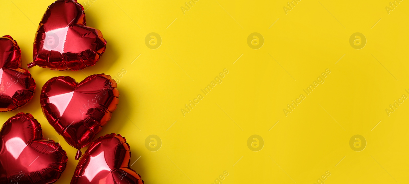 Photo of Red heart shaped balloons on yellow background, space for text. Valentine's Day celebration